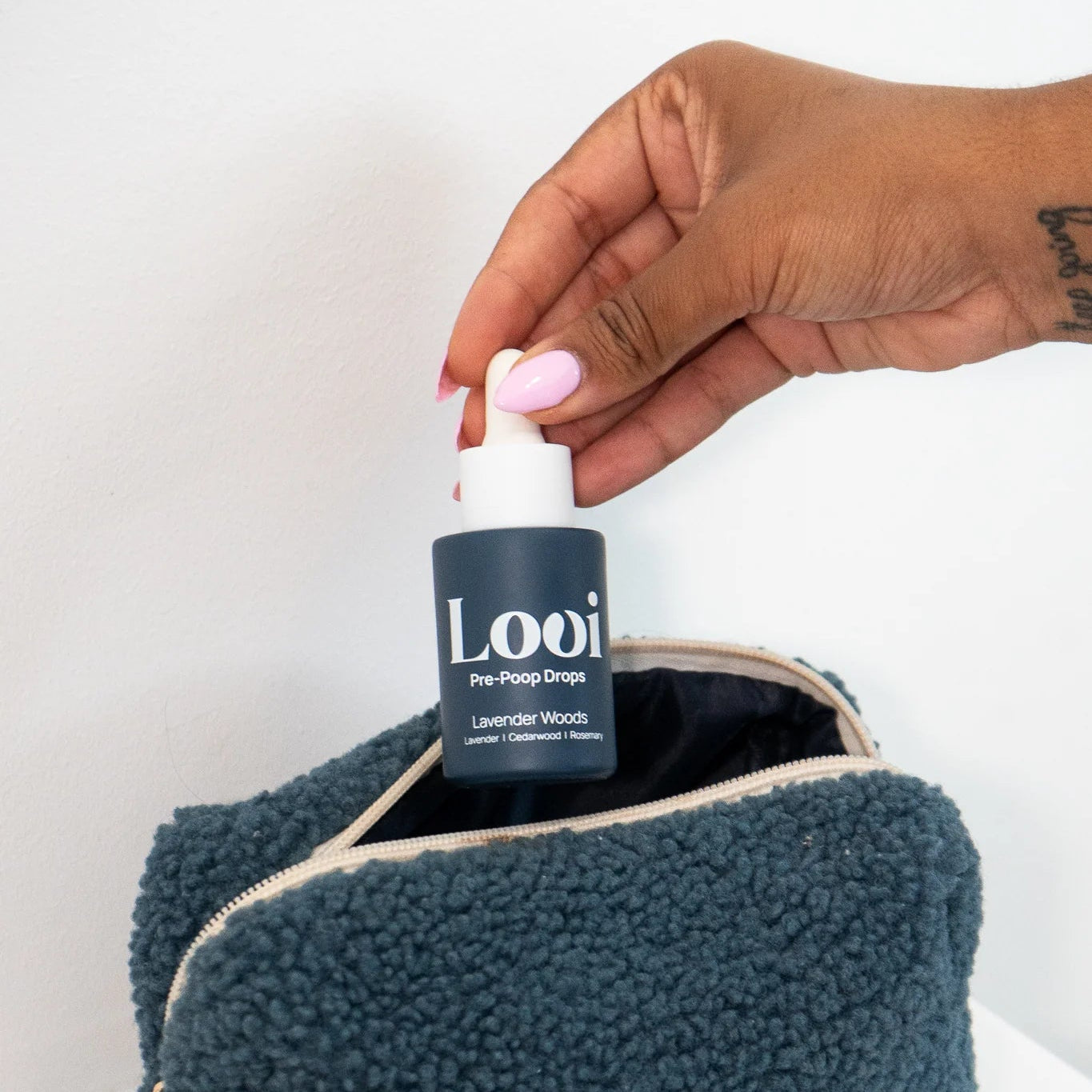 Hand holding a bottle labeled 'Loui' over a textured blue pouch on a white background