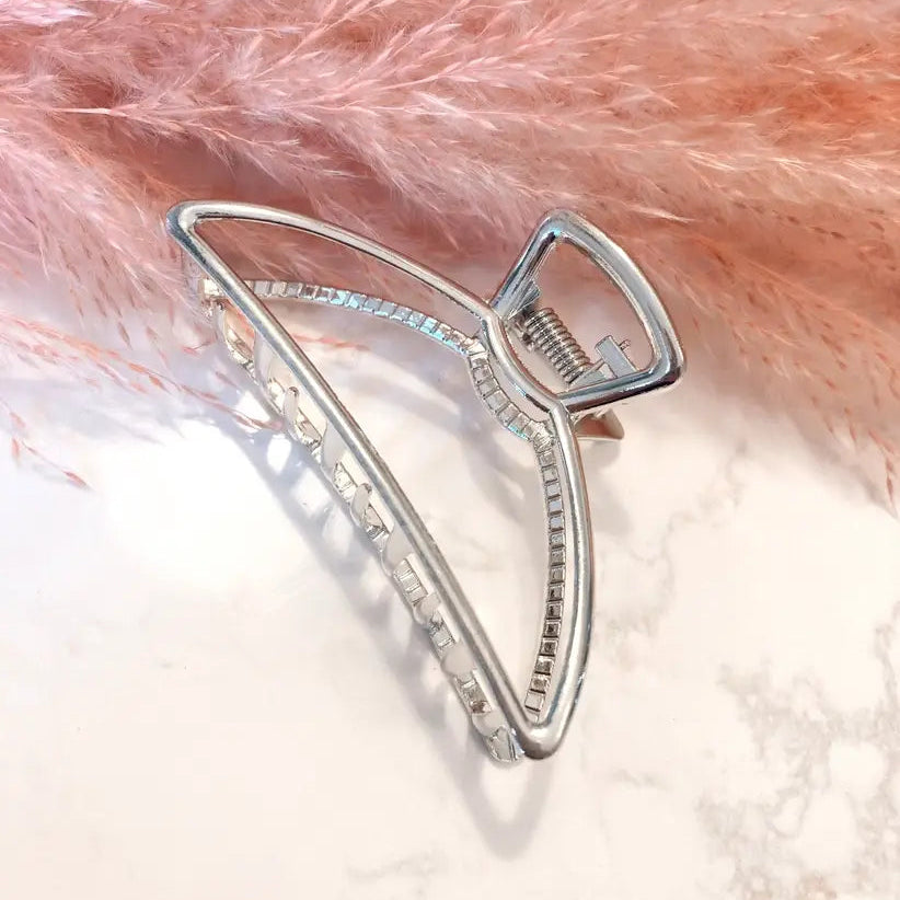 A silver metal claw hair clip resting on a pink fluffy faux-fur surface over a white marble background.