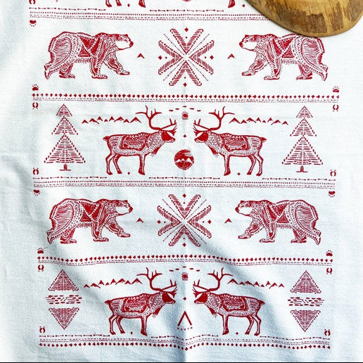 A white cotton tea towel with red Nordic-style patterns including a reindeer, a snowflake, and a tree.