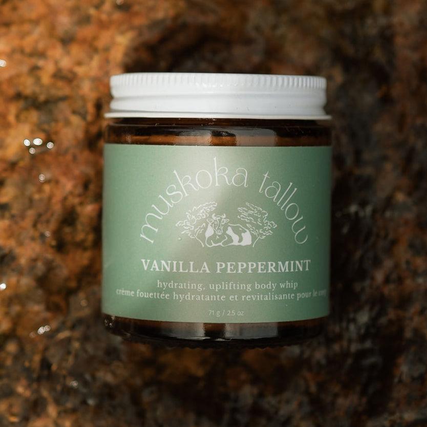 Jar of 'Vanilla Peppermint' body whip from Muskoka Tallow on a wet rocky surface