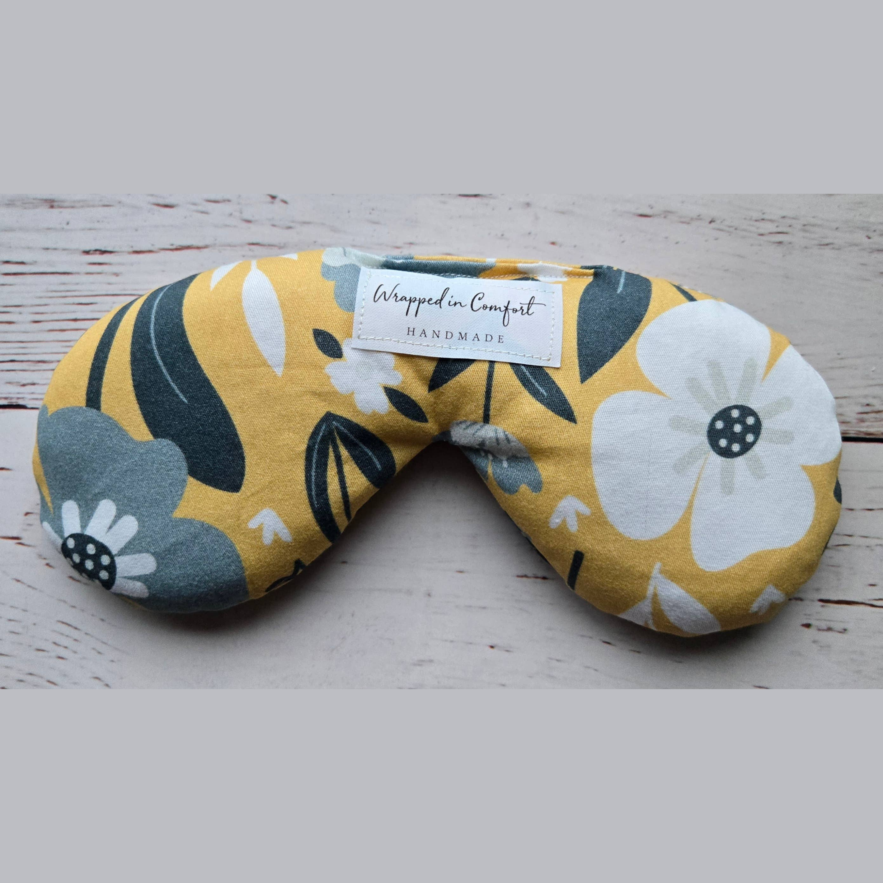 organic cotton bean shaped heating pad with floral-patterned fabric with a 'Wrapped in Comfort' label on a wooden surface
