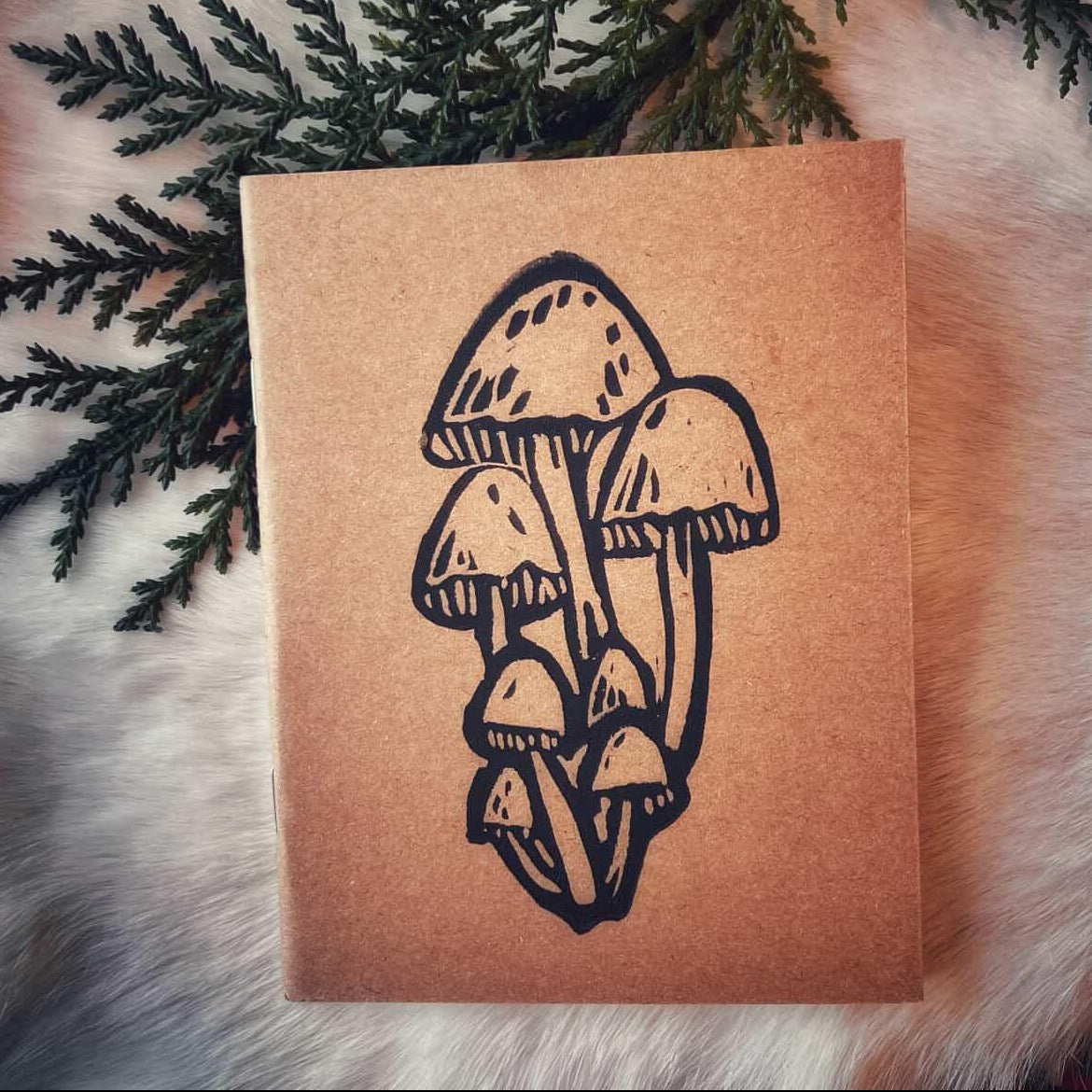 Notebook with mushroom design on a textured kraft paper surface with greenery and fur background.