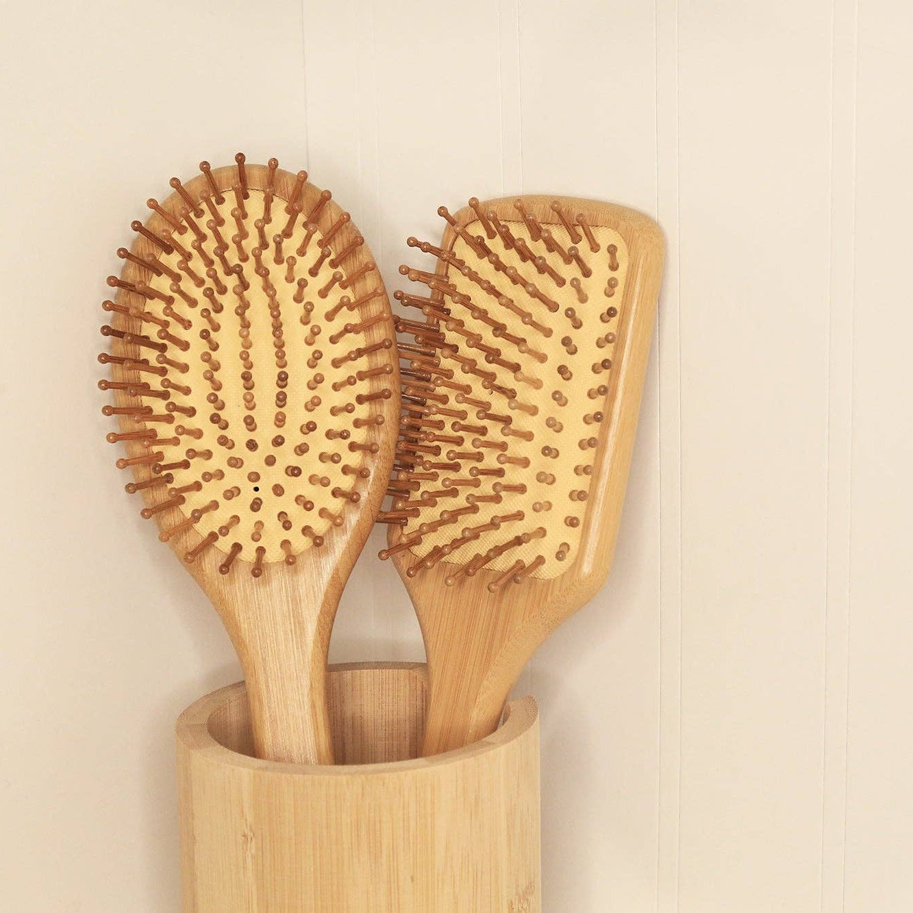 Two wooden hairbrushes in a cylindrical wooden holder on a beige background