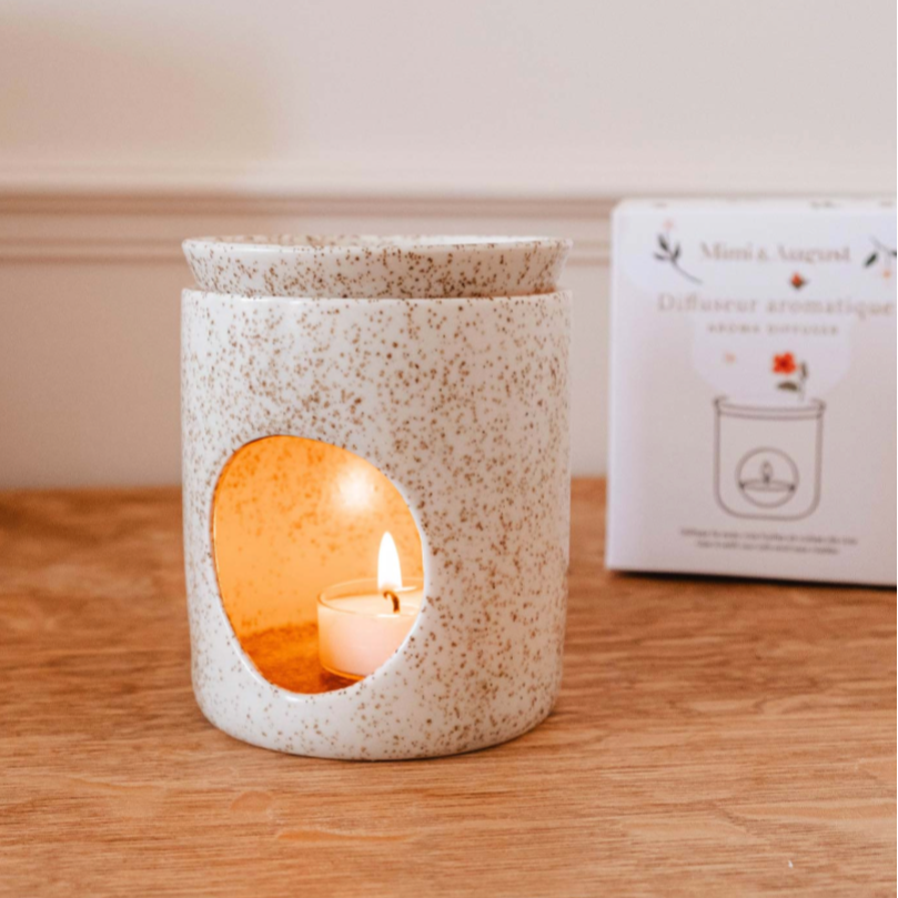 Speckled ceramic candle holder with a lit candle on a wooden surface, next to a product packaging.