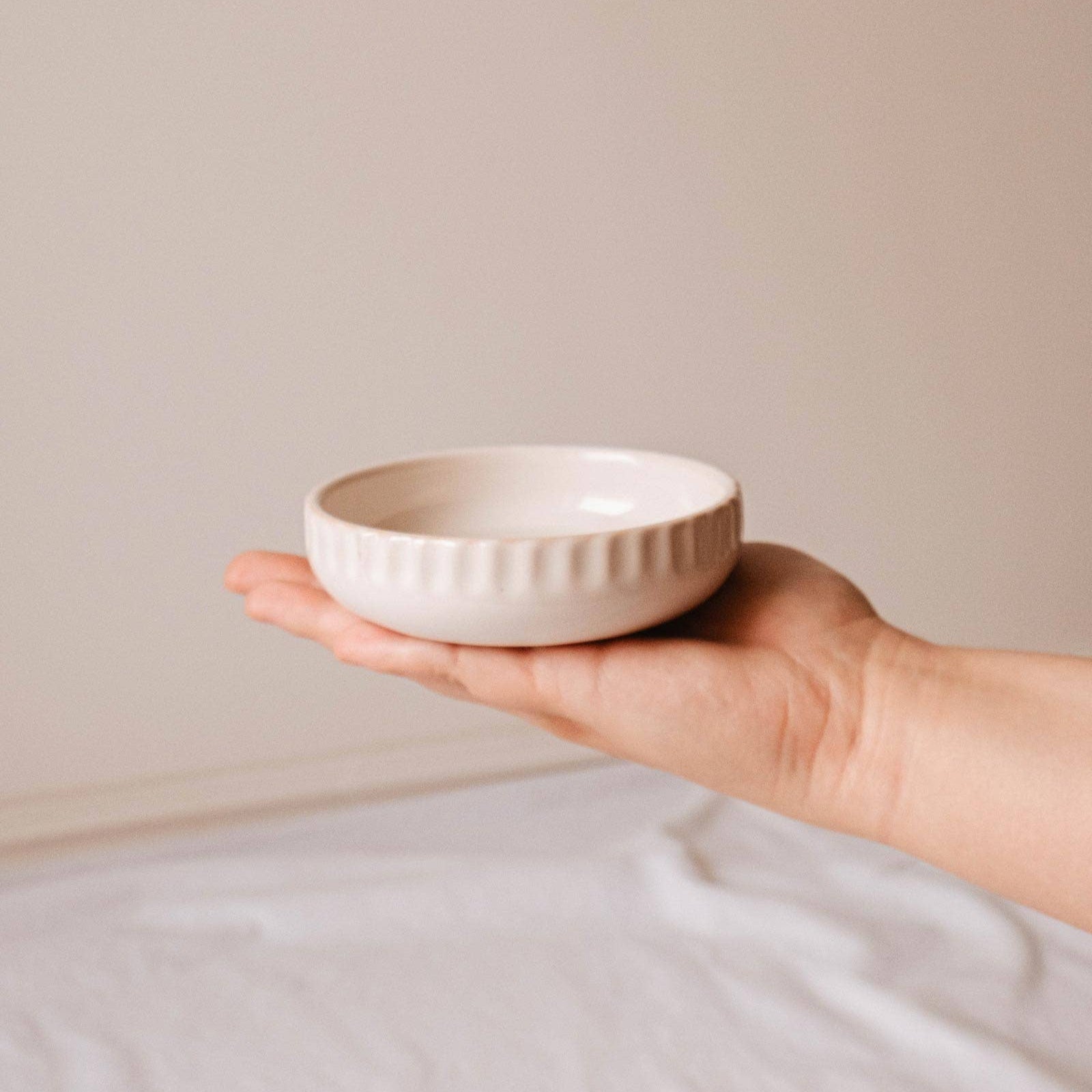 Hand holding a small ceramic bowl against a plain background