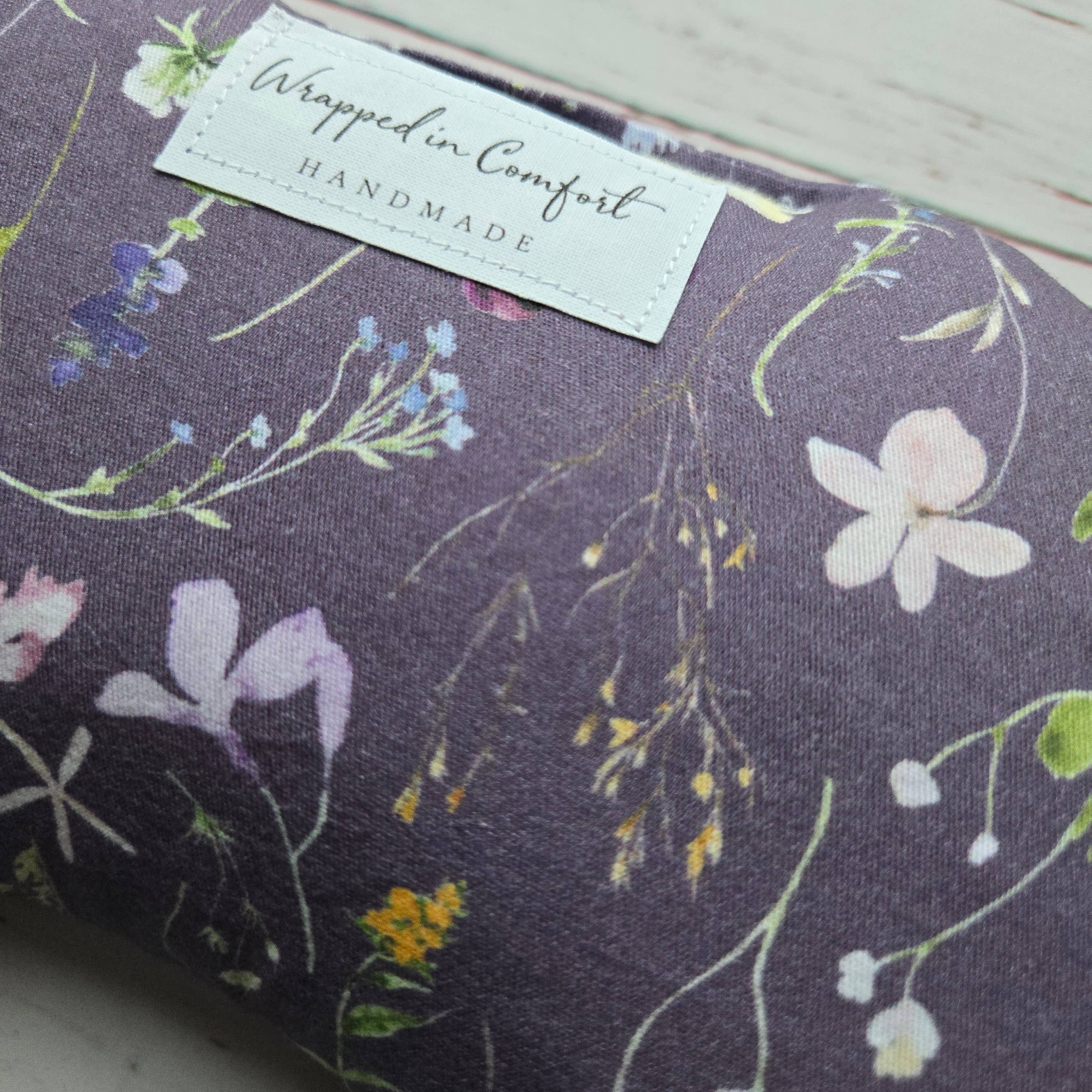organic cotton bean shaped heating pad with floral-patterned fabric with a 'Wrapped in Comfort' label on a wooden surface