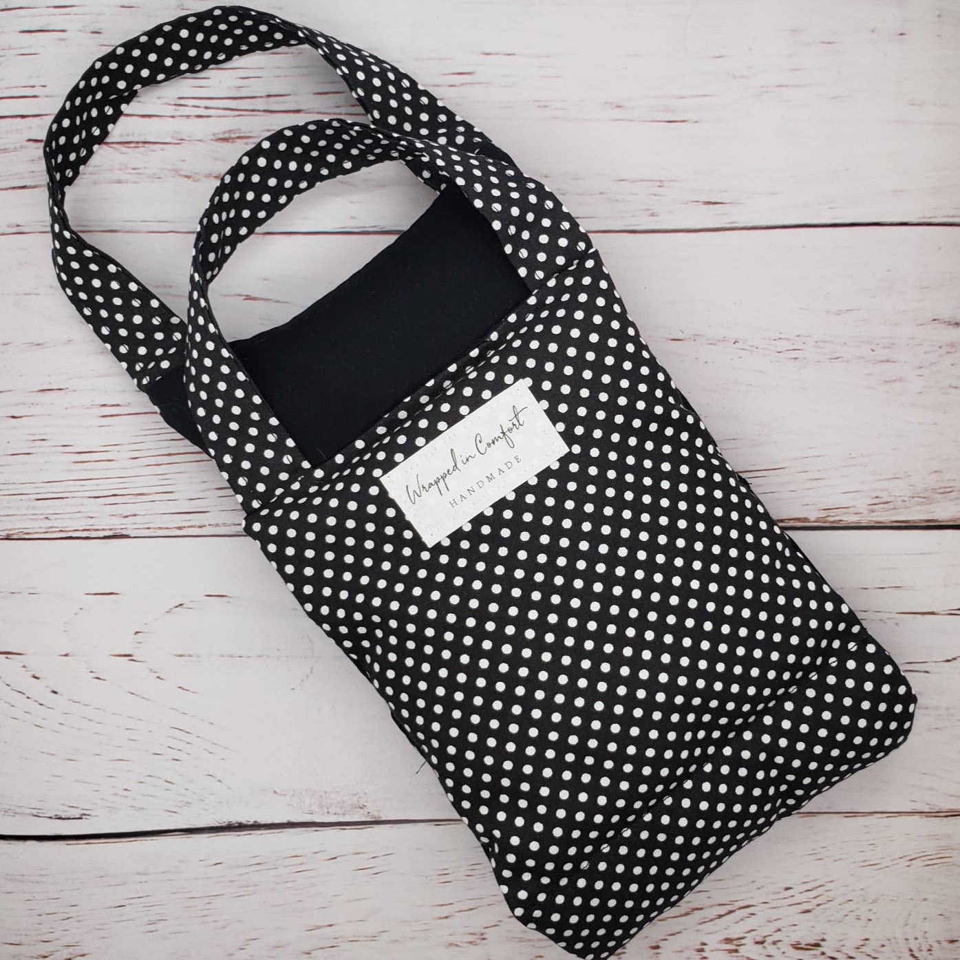 Black polka dot cotton neck heat wrap with handles on a light wooden surface.