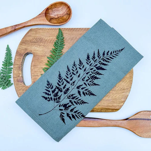 Teal napkin with leaf design on a wooden cutting board with a wooden spoon and fork.