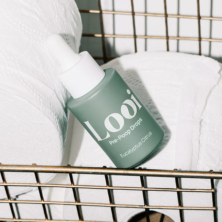 Green bottle labeled 'Loui' sitting on toilet paper rolls in a gold basket