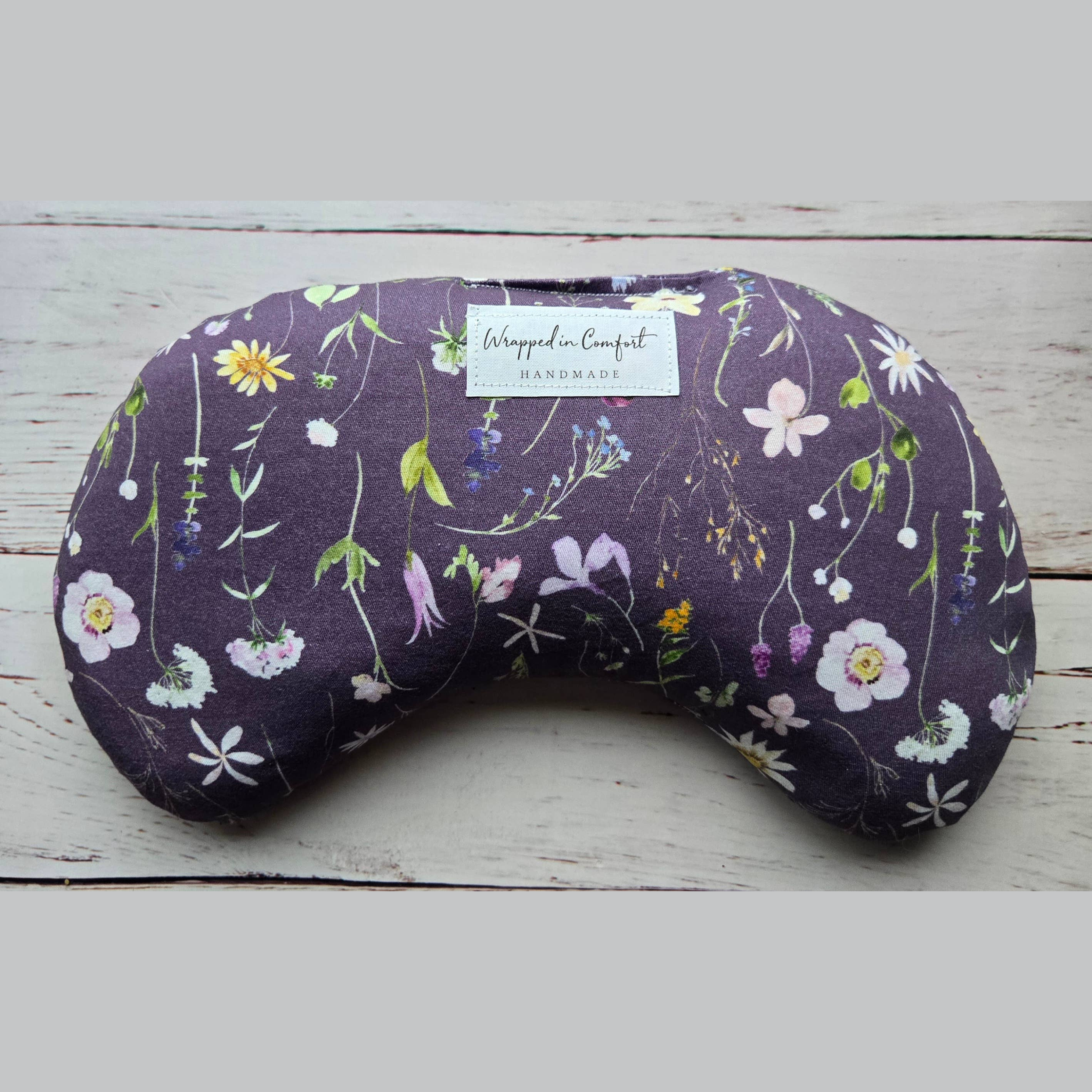 organic cotton bean shaped heating pad with floral-patterned fabric with a 'Wrapped in Comfort' label on a wooden surface