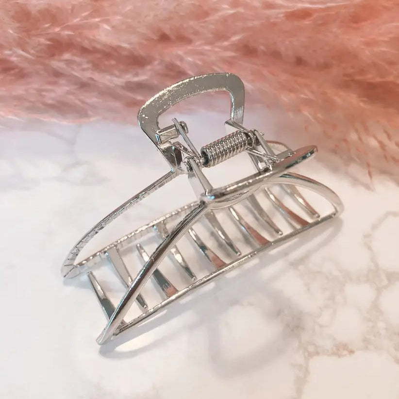 A silver metal claw hair clip resting on a white marble-patterned surface with a soft pink faux fur background.